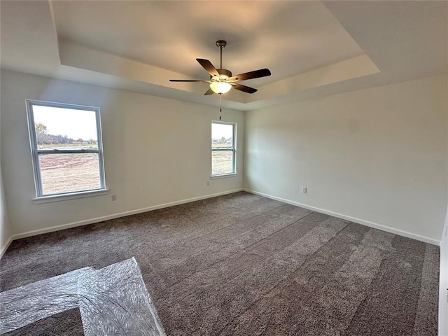 carpeted spare room featuring a tray ceiling, ceiling fan, and plenty of natural light