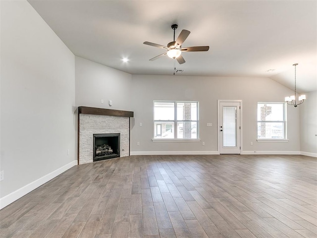 unfurnished living room with ceiling fan with notable chandelier, a healthy amount of sunlight, wood-type flooring, and a fireplace