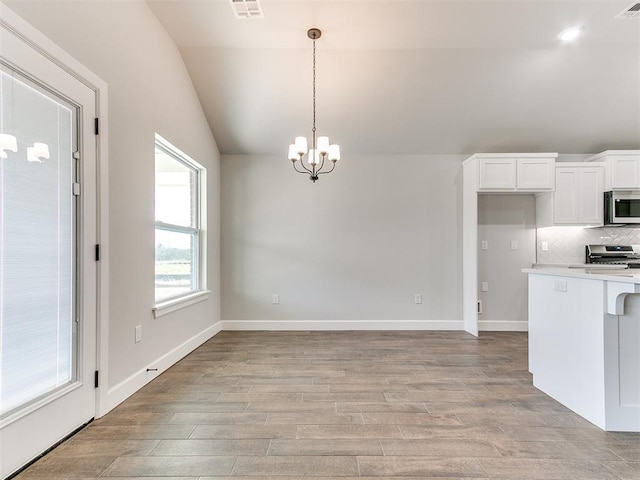 kitchen with stainless steel appliances, decorative light fixtures, light hardwood / wood-style floors, white cabinetry, and lofted ceiling