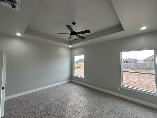 empty room with a raised ceiling, ceiling fan, and carpet