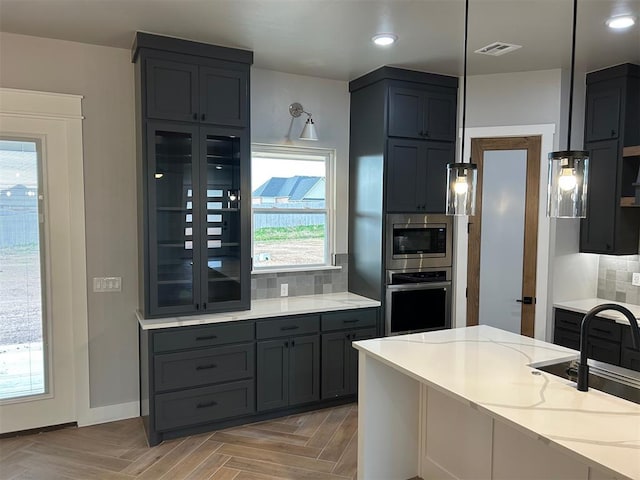 kitchen featuring tasteful backsplash, light stone counters, stainless steel appliances, pendant lighting, and light parquet flooring