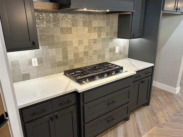 kitchen with gray cabinets, decorative backsplash, wall chimney range hood, and stainless steel gas stovetop