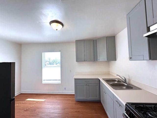 kitchen featuring gray cabinetry, sink, black appliances, and hardwood / wood-style flooring