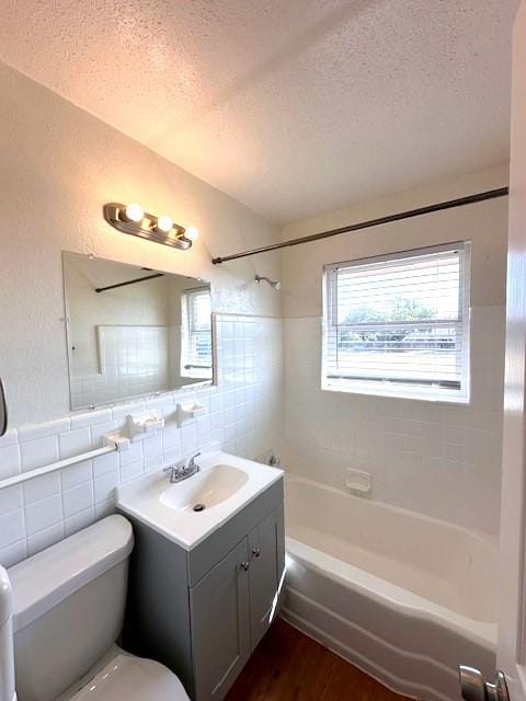 full bathroom with a textured ceiling, vanity, tiled shower / bath combo, and tile walls