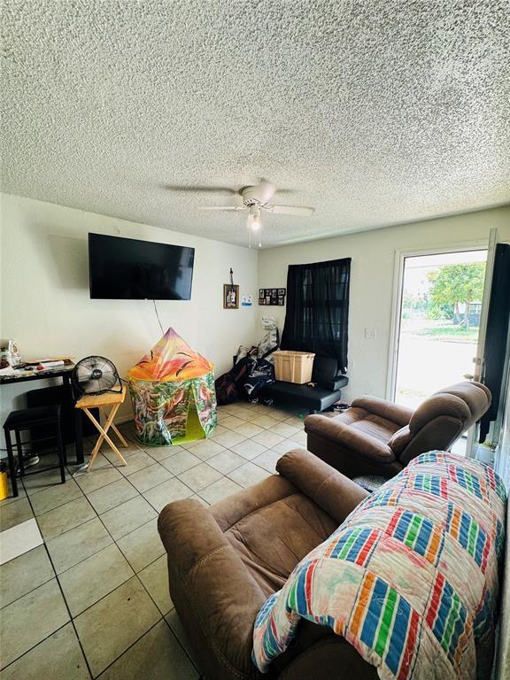 living room with light tile patterned flooring, ceiling fan, and a textured ceiling