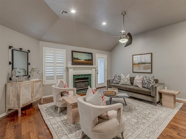 living room featuring lofted ceiling, a fireplace, visible vents, and wood finished floors