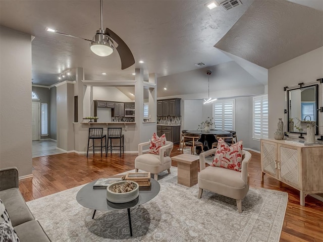 living room with a barn door, baseboards, visible vents, lofted ceiling, and light wood-style floors