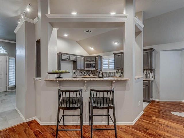 kitchen with gray cabinetry, a peninsula, a breakfast bar, visible vents, and built in microwave