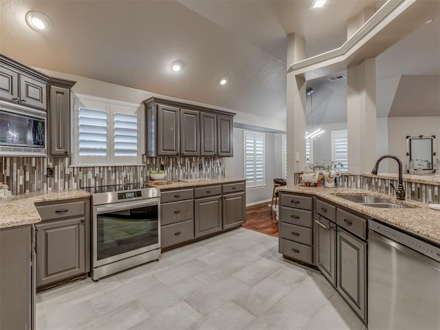 kitchen with a sink, vaulted ceiling, appliances with stainless steel finishes, light stone countertops, and tasteful backsplash