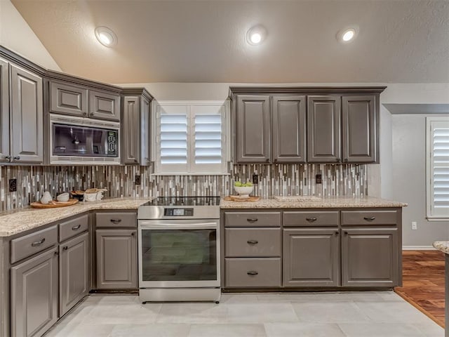 kitchen with black microwave, gray cabinetry, stainless steel range with electric cooktop, light stone countertops, and tasteful backsplash