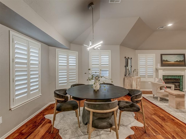 dining room featuring visible vents, vaulted ceiling, wood finished floors, a tile fireplace, and baseboards