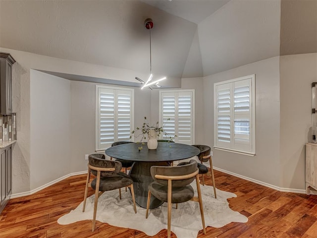 dining area featuring light wood-style floors, baseboards, and vaulted ceiling