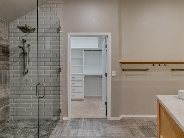 bathroom featuring a stall shower, baseboards, a walk in closet, and vanity