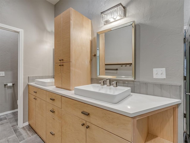 full bath with a textured wall, double vanity, and a sink