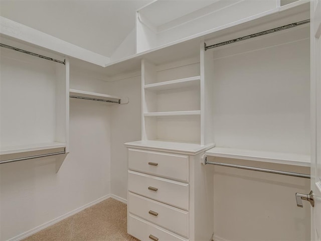 walk in closet featuring light colored carpet, vaulted ceiling, and a barn door