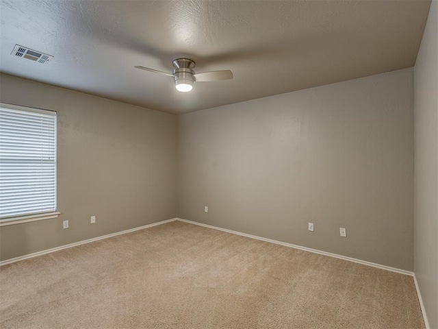 unfurnished room featuring a textured ceiling, light colored carpet, a ceiling fan, baseboards, and visible vents