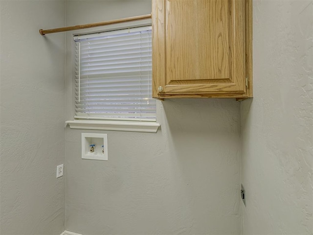 clothes washing area featuring cabinet space, washer hookup, and a textured wall