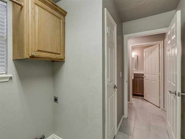 clothes washing area featuring cabinet space, a textured wall, electric dryer hookup, and light tile patterned floors