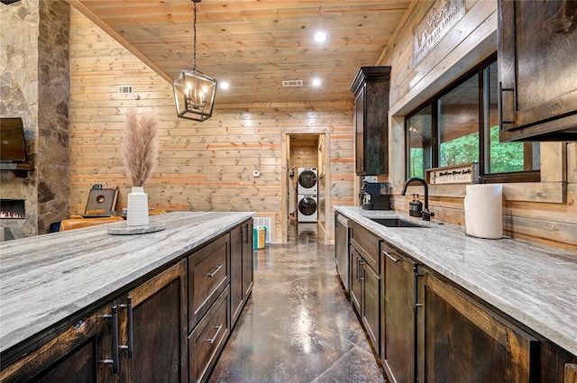 kitchen with decorative light fixtures, stacked washing maching and dryer, light stone counters, and wooden ceiling