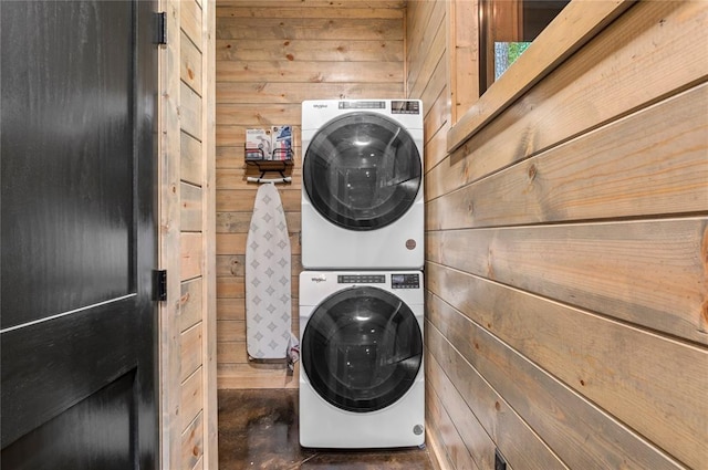 clothes washing area featuring stacked washing maching and dryer and wooden walls