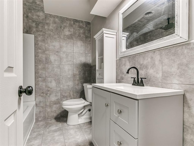 bathroom with vanity, tile patterned flooring, toilet, a tub to relax in, and tile walls