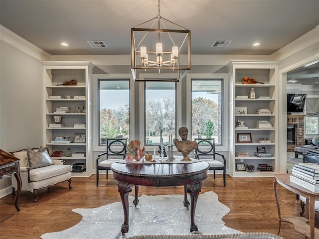 office with hardwood / wood-style floors, an inviting chandelier, a brick fireplace, built in shelves, and ornamental molding