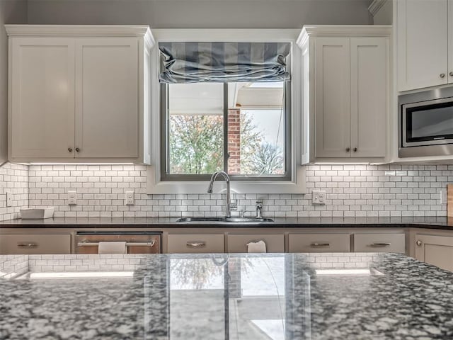 kitchen featuring appliances with stainless steel finishes, backsplash, sink, dark stone countertops, and white cabinets