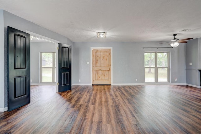 unfurnished living room featuring a textured ceiling, dark wood-type flooring, ceiling fan, and a healthy amount of sunlight