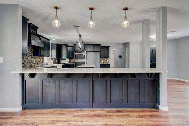 kitchen featuring decorative backsplash, pendant lighting, light hardwood / wood-style floors, and appliances with stainless steel finishes