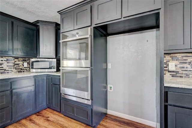 kitchen featuring decorative backsplash, light wood-type flooring, stainless steel appliances, and light stone counters