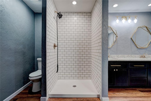 bathroom featuring a tile shower, vanity, hardwood / wood-style flooring, and toilet