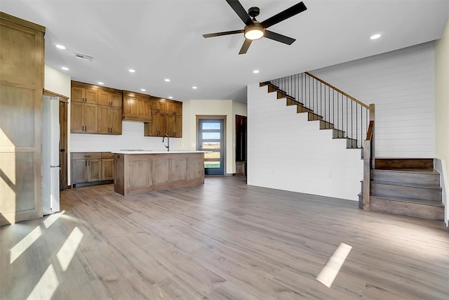 kitchen with a kitchen island with sink, ceiling fan, white refrigerator, and light wood-type flooring