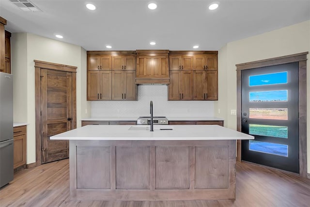 kitchen with stainless steel refrigerator, sink, light hardwood / wood-style floors, a kitchen island with sink, and custom range hood