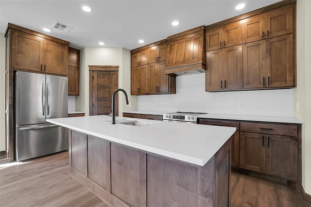 kitchen with light hardwood / wood-style flooring, sink, stainless steel appliances, and an island with sink