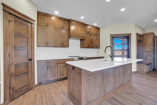 kitchen featuring sink, electric stove, a kitchen island with sink, custom range hood, and light wood-type flooring