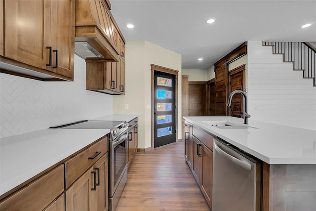 kitchen with backsplash, premium range hood, sink, light hardwood / wood-style flooring, and stainless steel appliances