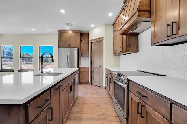 kitchen featuring custom exhaust hood, sink, light hardwood / wood-style flooring, decorative backsplash, and stainless steel appliances