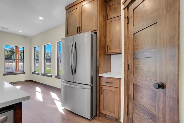 kitchen with tasteful backsplash, stainless steel refrigerator, and light hardwood / wood-style flooring