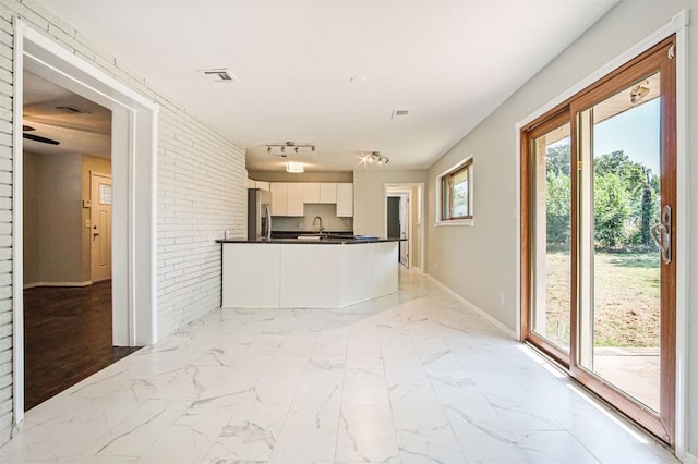 kitchen with stainless steel fridge, sink, white cabinets, and brick wall