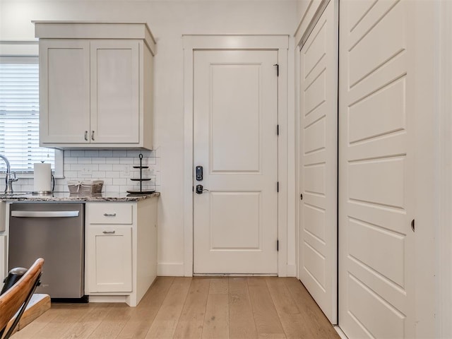 bar featuring dishwasher, tasteful backsplash, light hardwood / wood-style flooring, and dark stone countertops