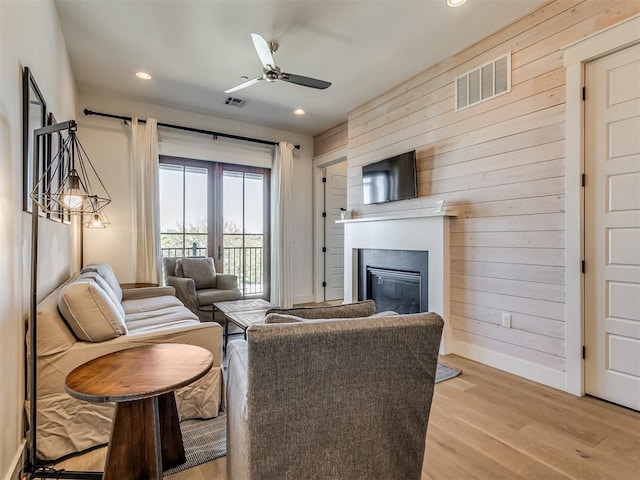 living room with ceiling fan, light hardwood / wood-style flooring, and wooden walls