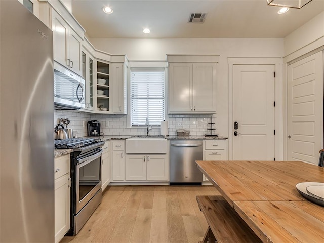 kitchen with dark stone counters, white cabinets, sink, light hardwood / wood-style flooring, and stainless steel appliances