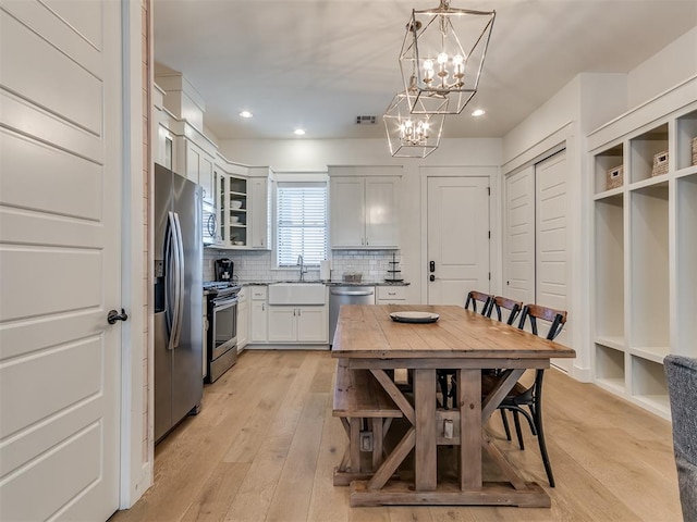 kitchen featuring hanging light fixtures, white cabinets, stainless steel appliances, and light wood-type flooring