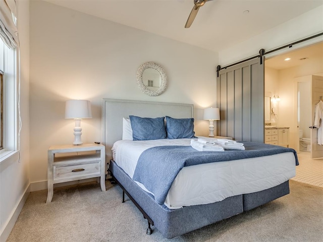 carpeted bedroom with a barn door, ensuite bathroom, and ceiling fan