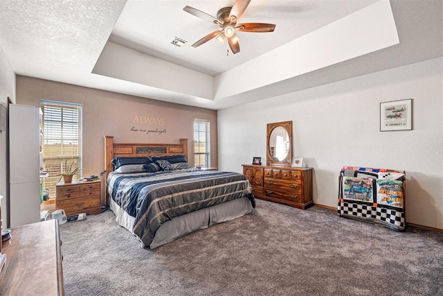 carpeted bedroom featuring a raised ceiling, multiple windows, ceiling fan, and a textured ceiling