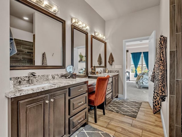 ensuite bathroom featuring wood finish floors, double vanity, a sink, ensuite bath, and baseboards