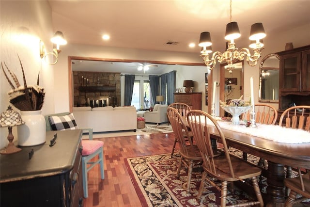 dining room featuring ceiling fan with notable chandelier, dark hardwood / wood-style floors, and a stone fireplace