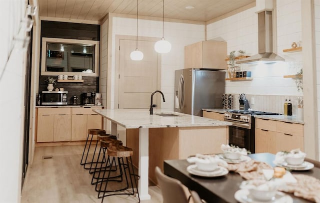 kitchen featuring light stone counters, an island with sink, decorative light fixtures, island range hood, and appliances with stainless steel finishes