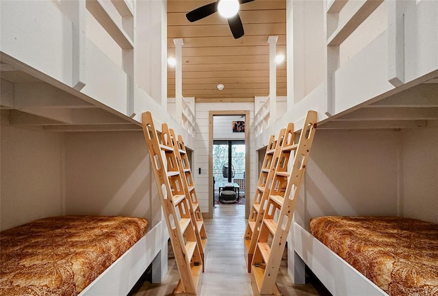 bedroom with ceiling fan, light wood-type flooring, and wooden walls