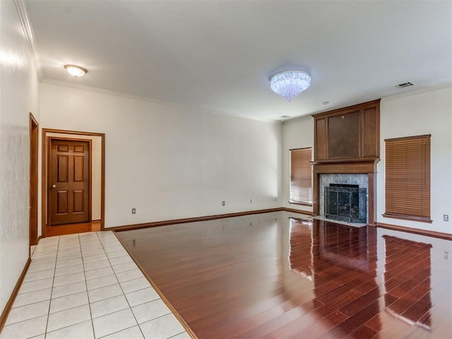 unfurnished living room with crown molding, an inviting chandelier, a premium fireplace, and light wood-type flooring